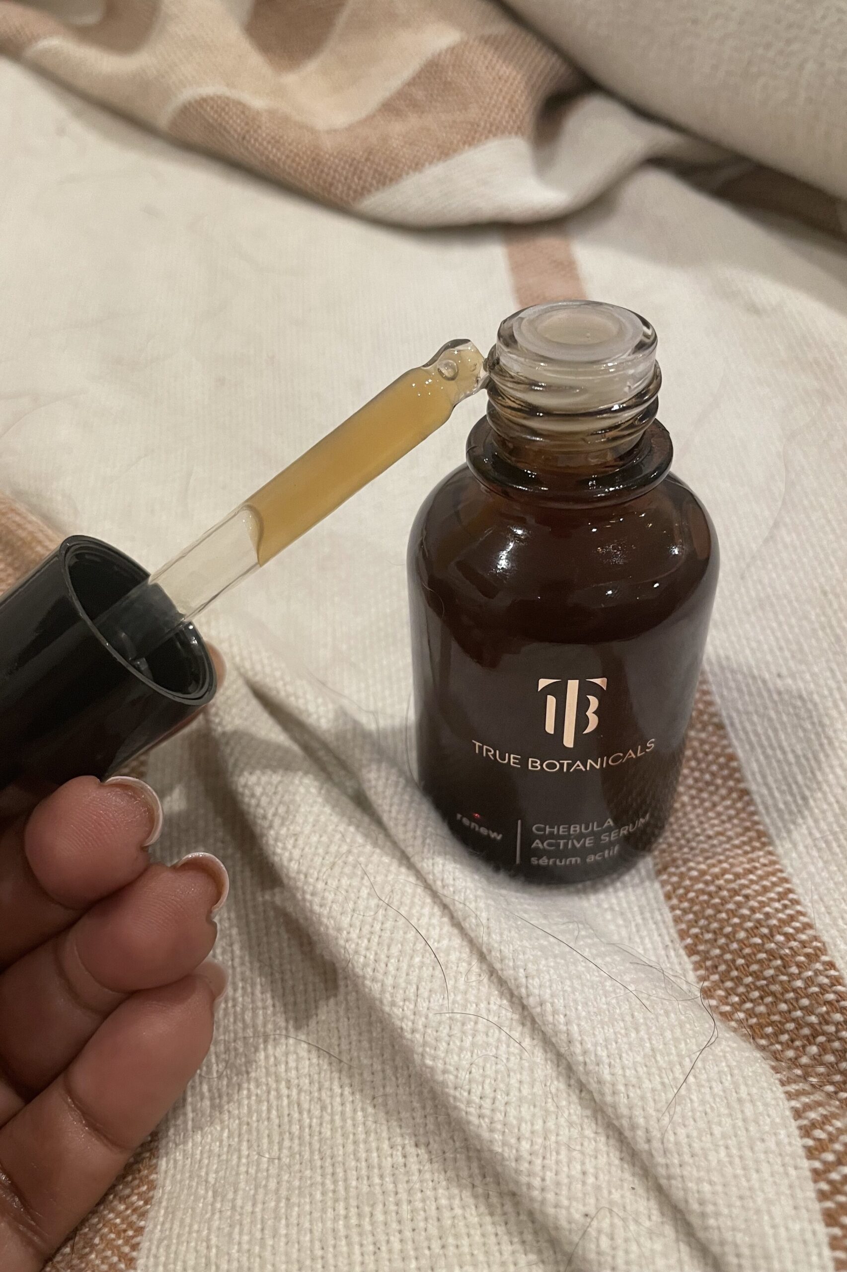 A person holding a bottle of true botanicals cbd oil on a bed.