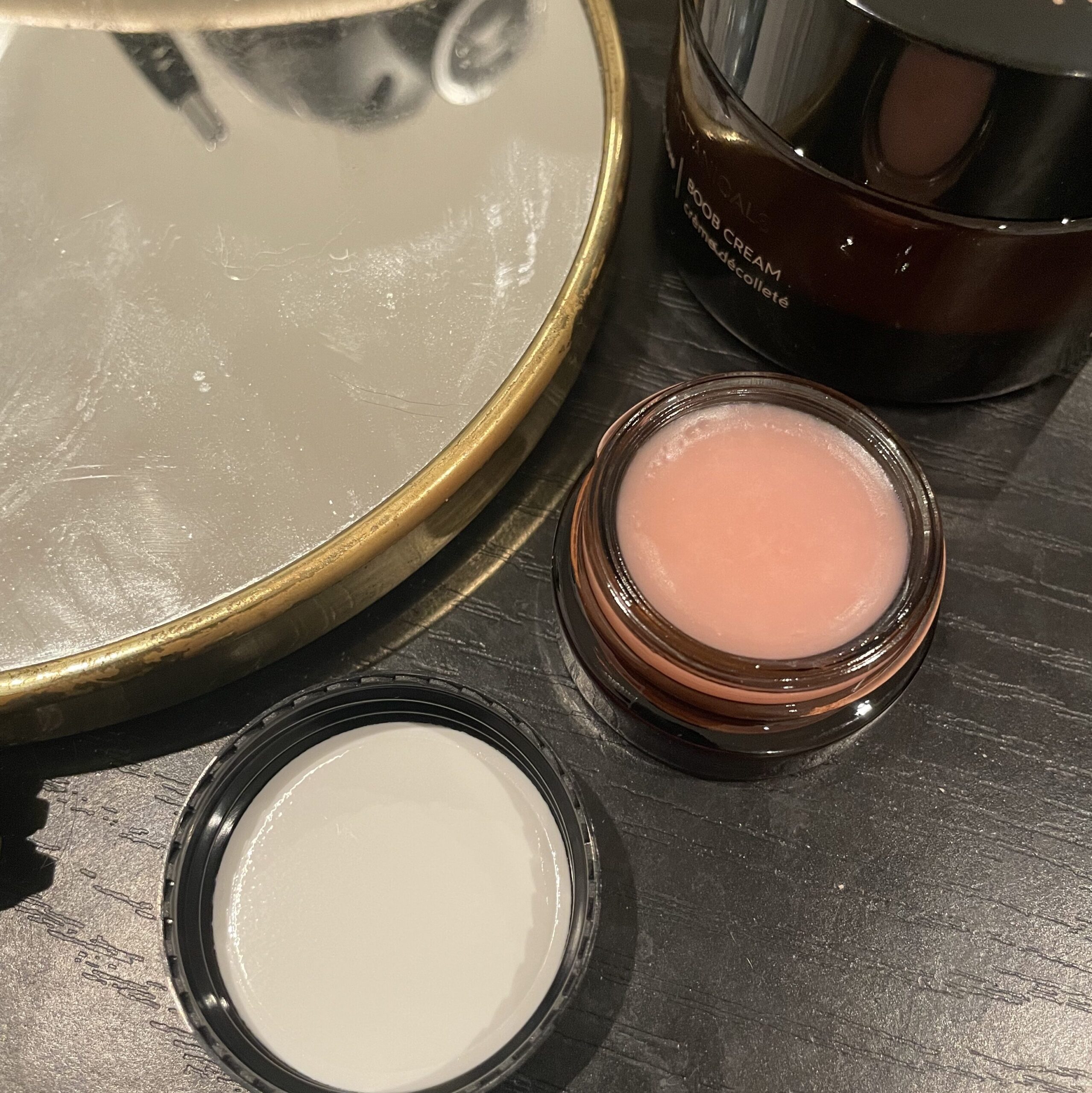 A jar of True Botanicals lip balm on a table next to a mirror.