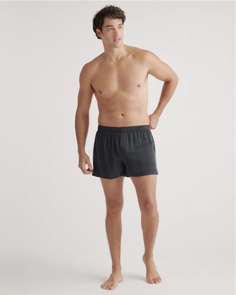 A shirtless man stands in front of a plain background wearing black shorts.
