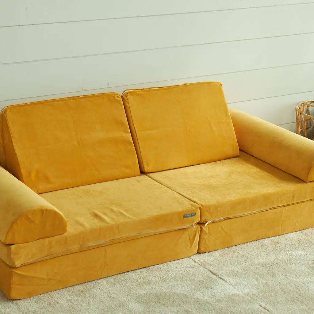 Yellow sofa with two large cushions on a cream carpet, against a white paneled wall.