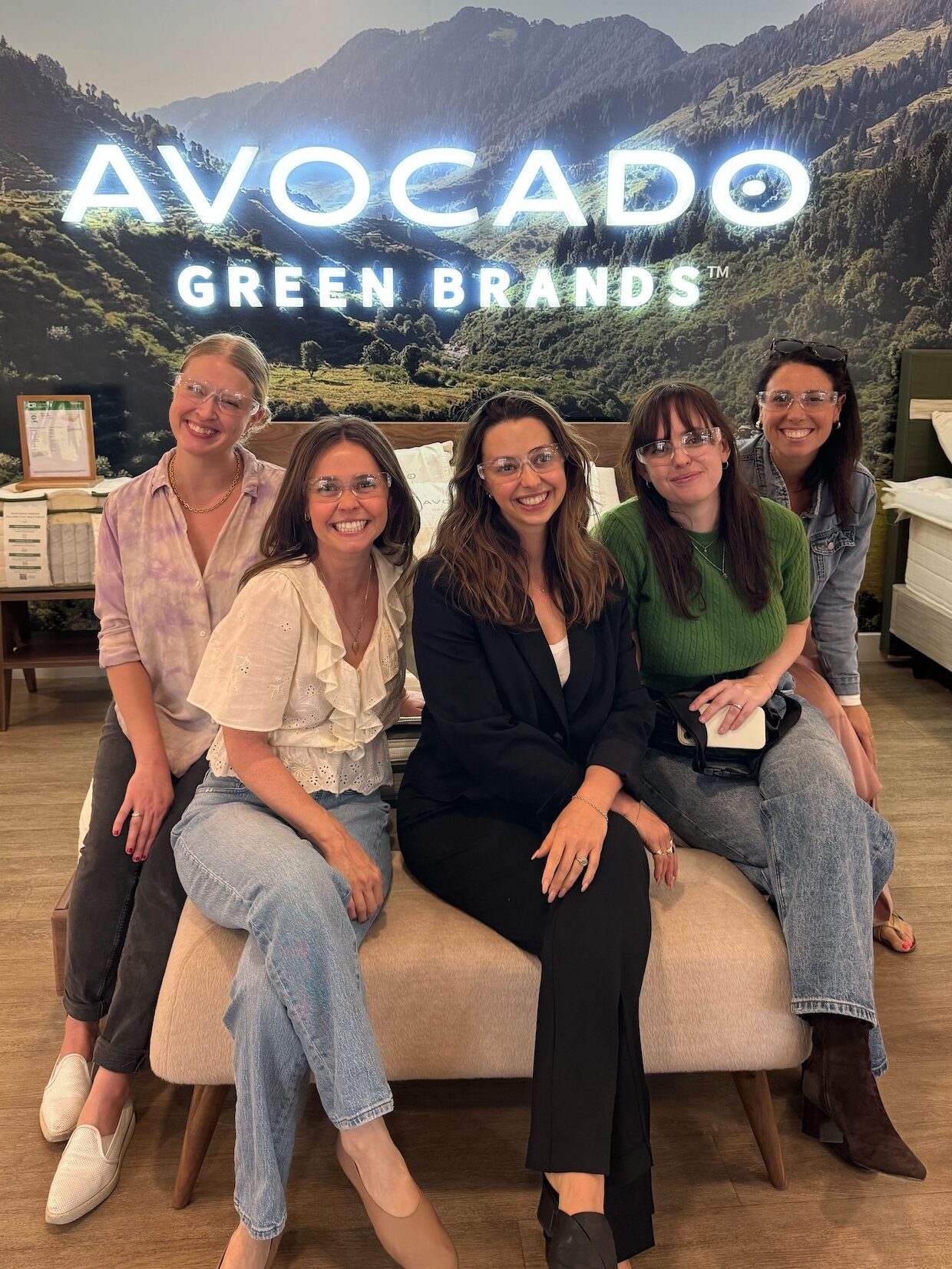 Five members of AlsWell Blog team wearing safety glasses pose on a bench in front of an "Avocado Green Brands" sign at the brand's factory in Fullerton California.