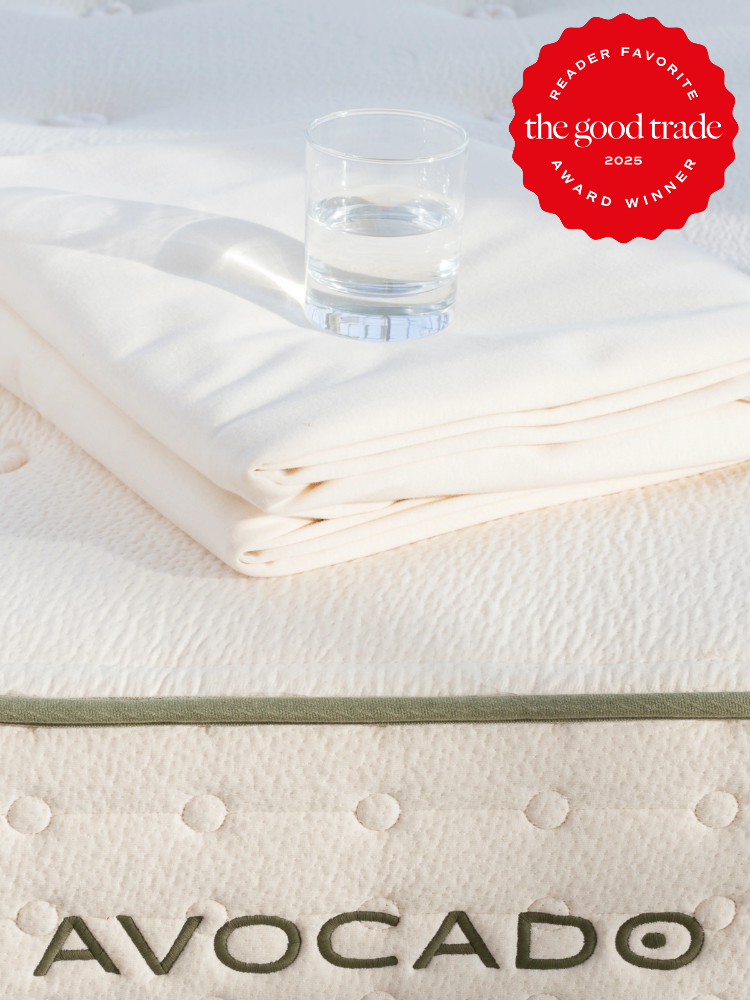 A glass of water on folded white linens atop an Avocado mattress. A red badge reads "Reader Favorite, AlsWell Blog Award Winner 2025.