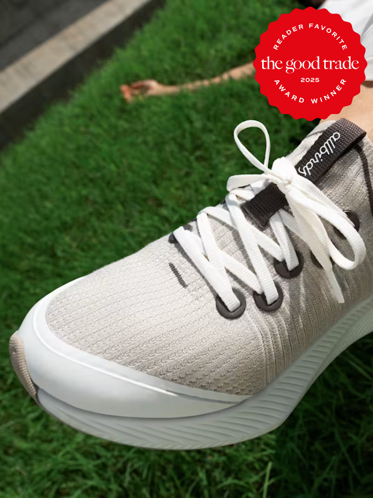 Close-up of a person wearing light gray sustainable sneakers on grass, with a red "AlsWell Blog 2025 Reader Favorite Award Winner" badge in the upper right corner.
