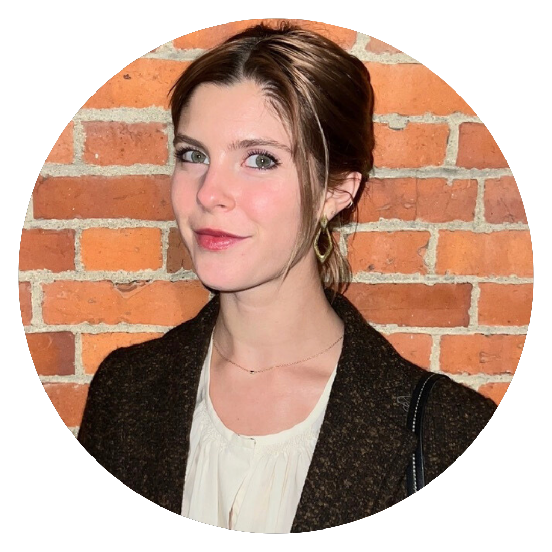A woman with brown hair, light skin, and green eyes stands in front of a brick wall, wearing a white blouse, dark coat, and gold hoop earrings—holding a brochure about choosing the perfect latex mattress.